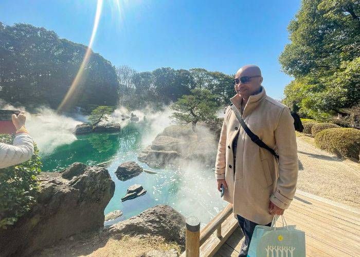 A smiling guest on the Fukuoka city tour, standing next to hot springs on a clear day.